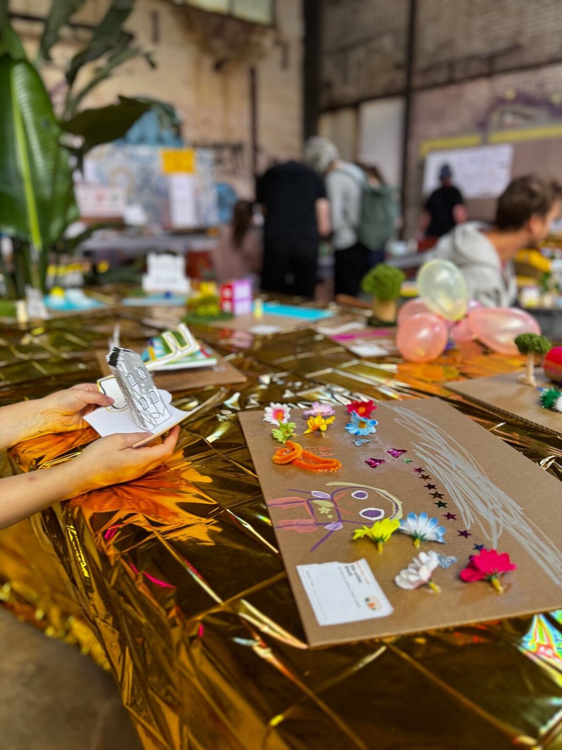 Hände halten ein Haus aus Papier über einem Modell aus Pappe und Goldfolie