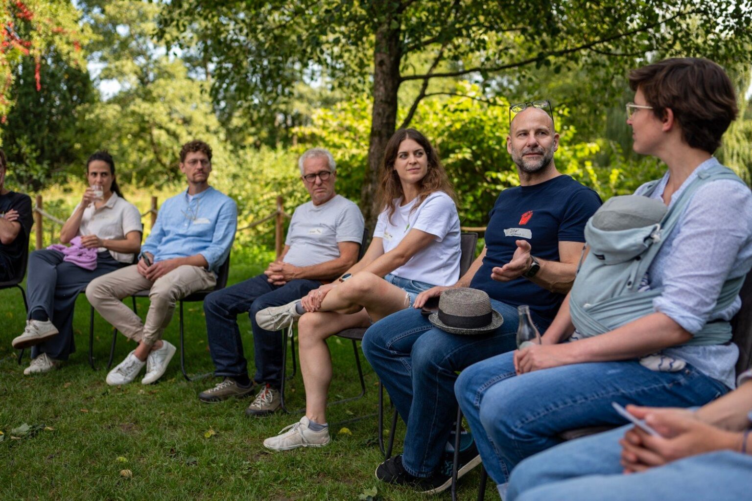 Menschen sitzen im Stuhlkreis auf einer Wiese unter Bäumen, Jan Schmirmund erzählt, die anderen hören zu